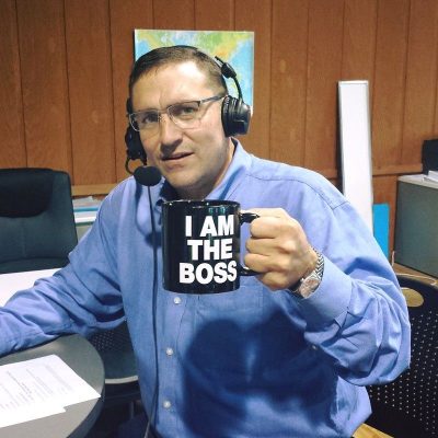 CEO Jeffrey Potter in radio studio wearing headsets with boom mic holding coffee mug which says I AM THE BOSS