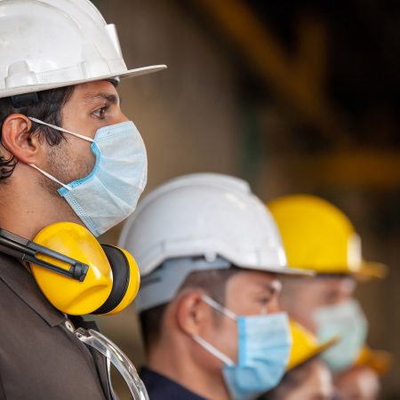 workers wear protective face masks and hard hats in industrial setting